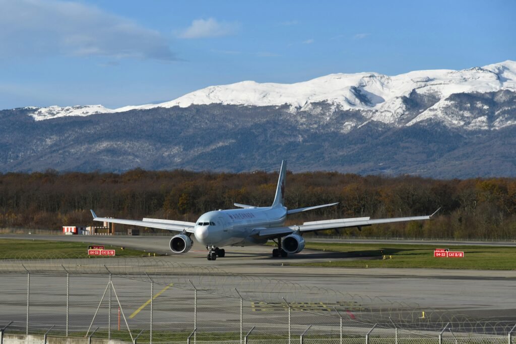 Commercial aircraft taxiing on the runway at Geneva Airport with a mountain backdrop.